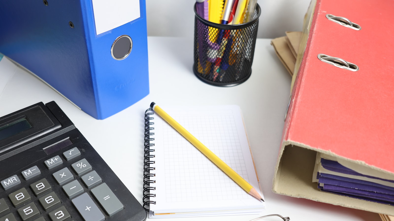 Desk with calculator, binders, notebook, and glasses